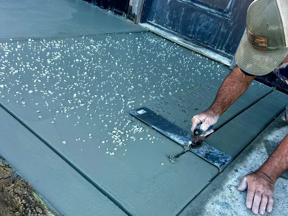 Hands running a steel trowel along the edge of a wet concrete slab